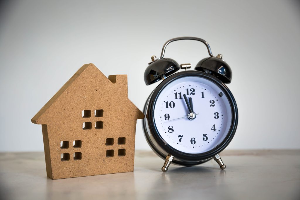 Model house next to a clock representing delays caused by financing approvals